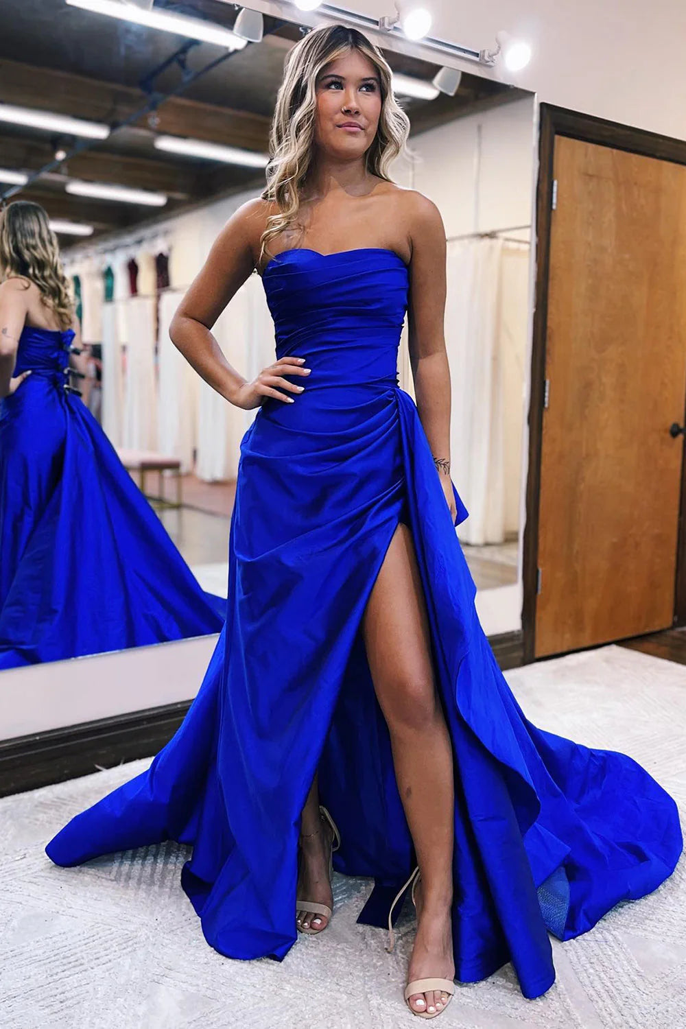 Woman wearing an elegant strapless sheath long prom dress with a high slit.