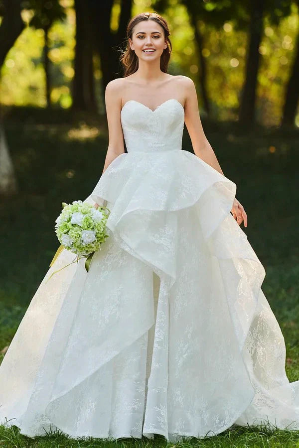 Elegant white sweetheart lace bridal ball gown with an open back and cascading ruffles.