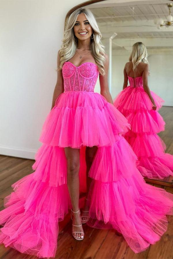 Woman posing in a hot pink high-low tiered prom dress with a sweetheart V-neckline.