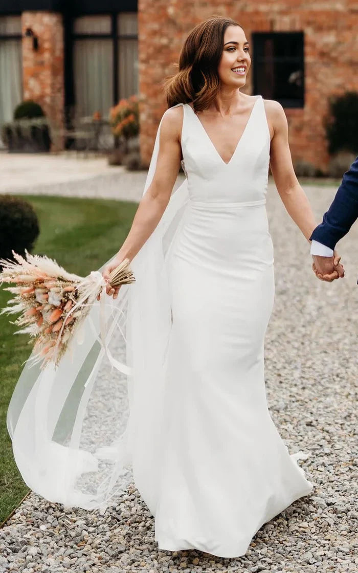 Woman wearing an elegant white trumpet V-neck wedding dress with a long train.