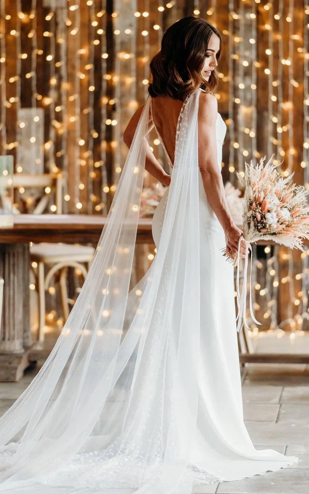 Back view of a woman in a white trumpet V-neck wedding dress, showing the V back and long train.