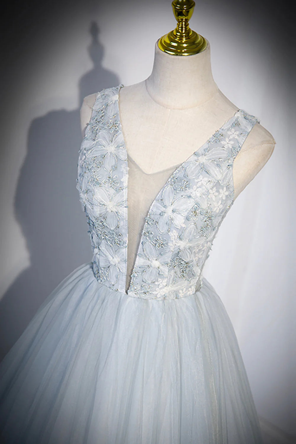 Model in a long tulle V-neck prom dress, standing elegantly with hands clasped.