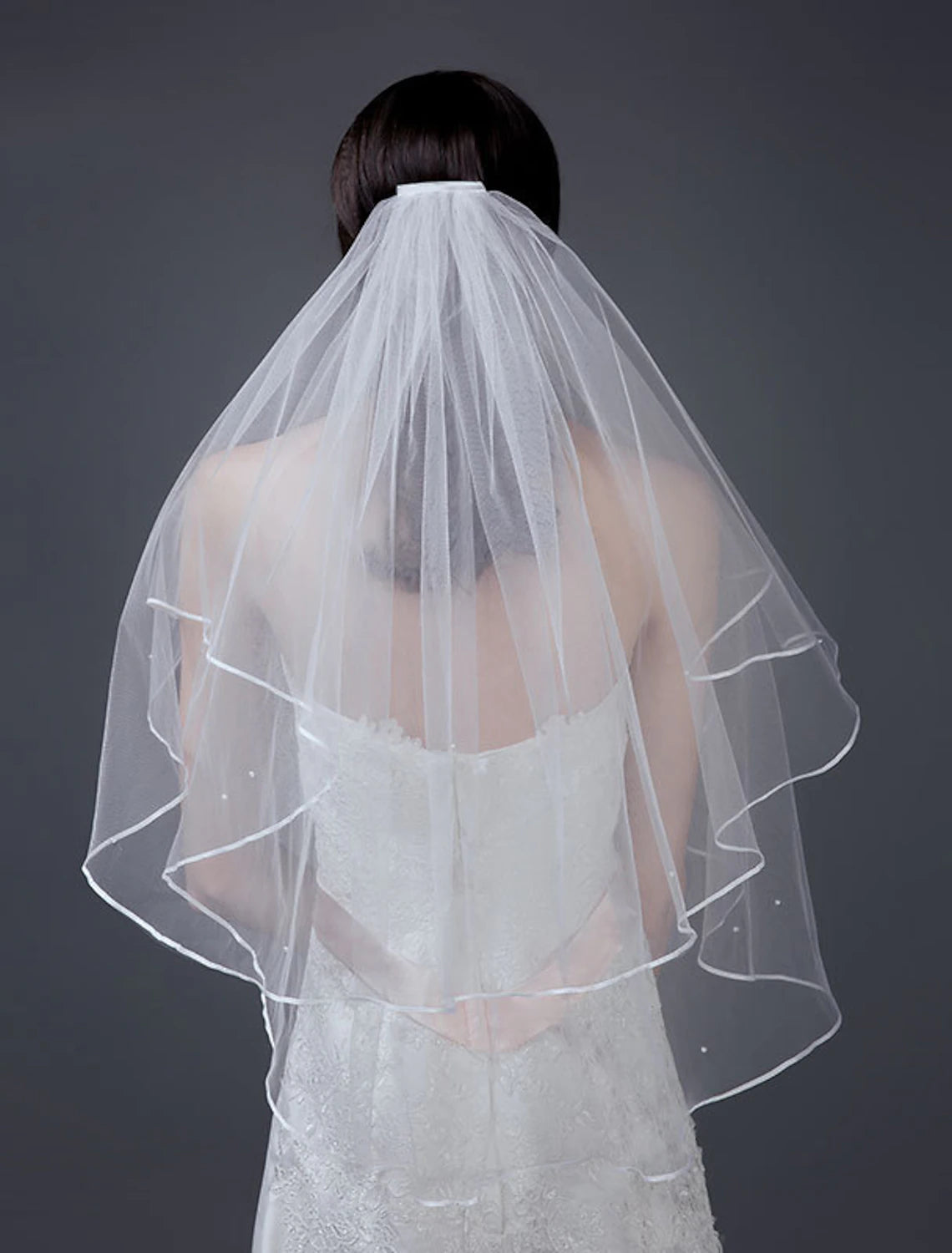 A bride wearing a two-layer short white bridal veil with a comb edge.