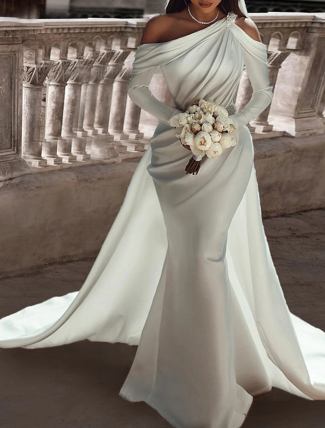 Model wearing a two-piece one-shoulder long-sleeve satin wedding dress with a sash and beading, front view.