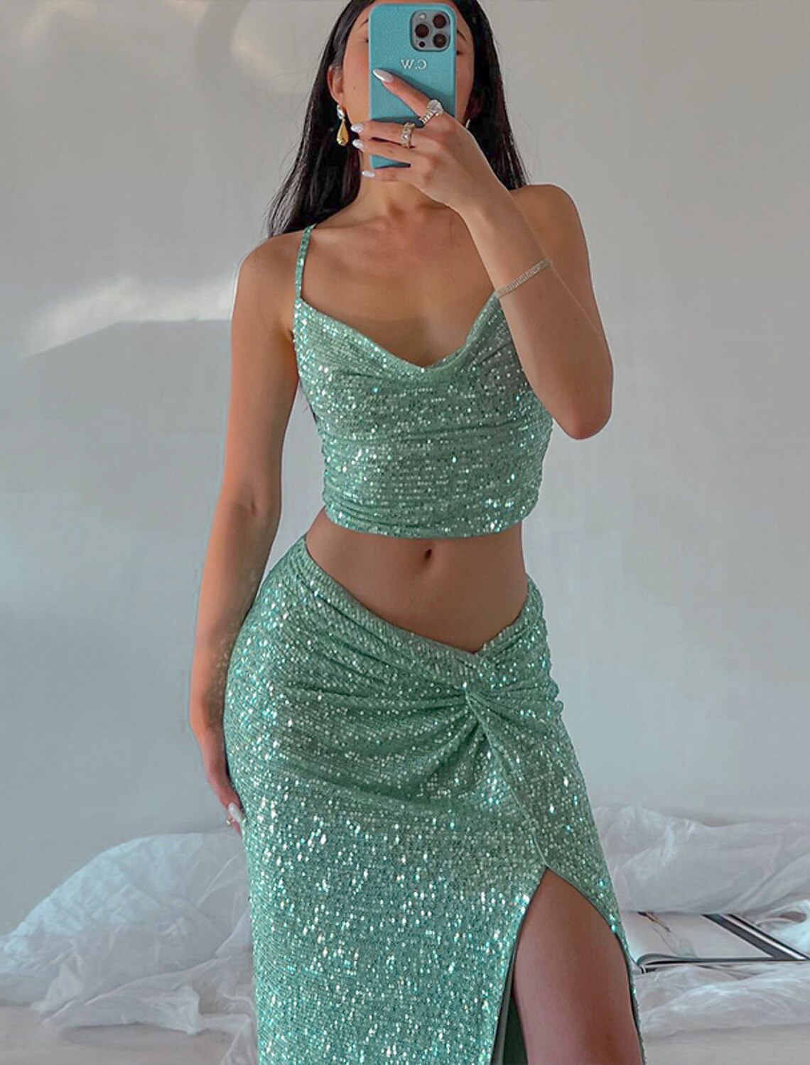 Model wearing an elegant dark sequin two-piece floor-length party dress with spaghetti straps and a high slit.