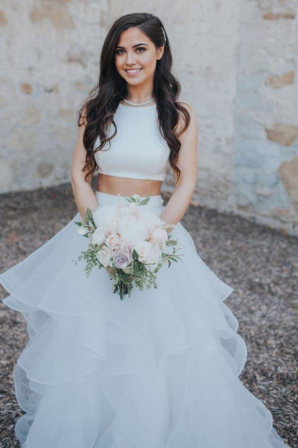 Model wearing an elegant two-piece white wedding dress with a V-neck top and ruffled A-line skirt.