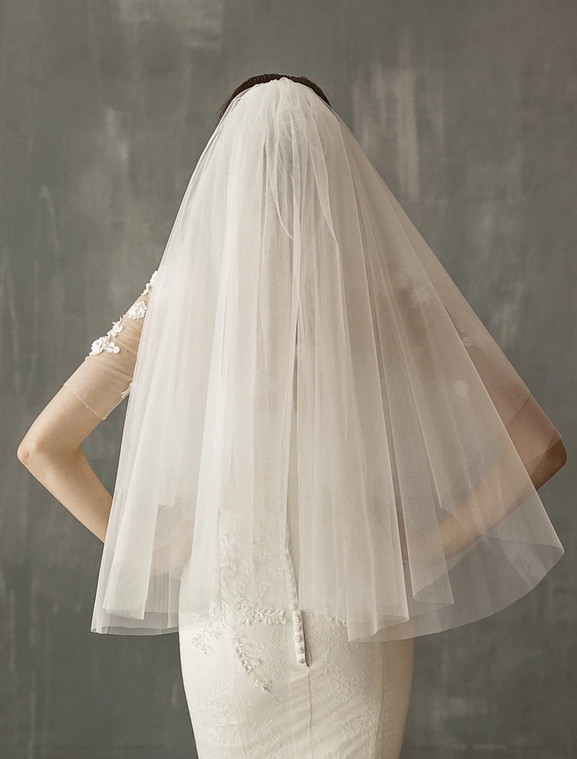 Close-up of a bride's back, showing the graceful drape of a two-tier tulle wedding veil.