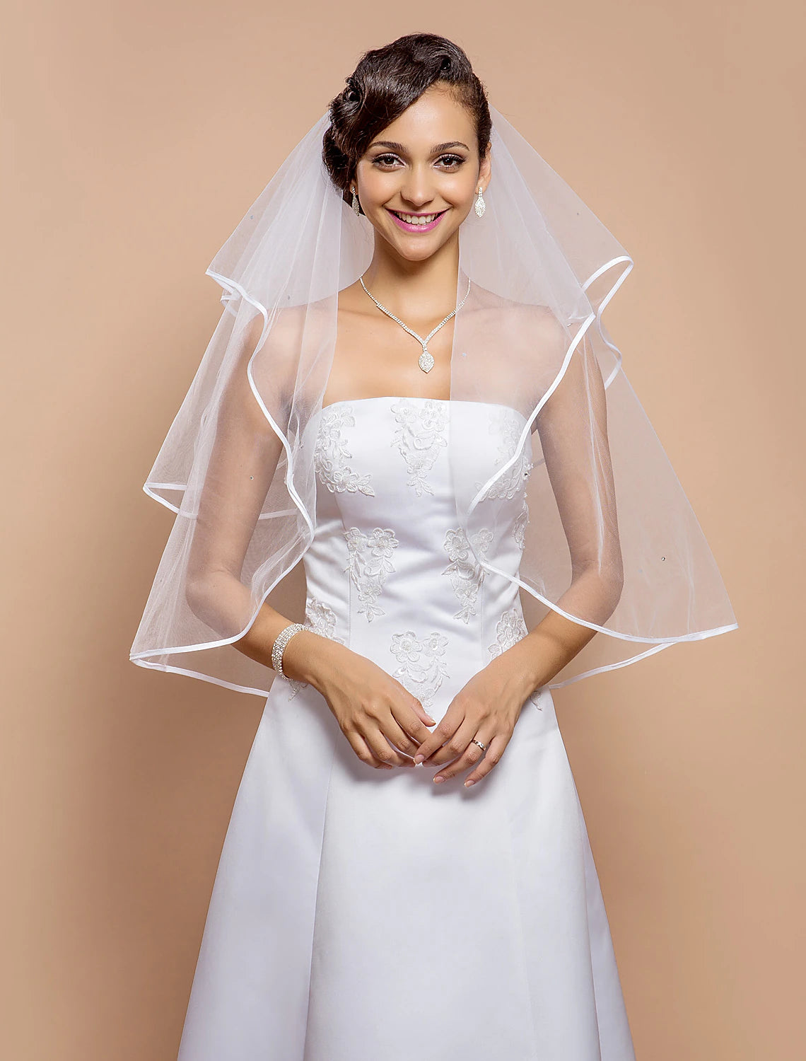Bride wearing an elegant two-tier wedding veil with ribbon edge and sparkling rhinestones.