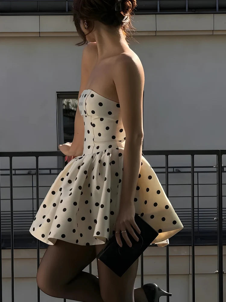 Model wearing a white V-neck A-line mini dress with black polka dots and a bow detail.