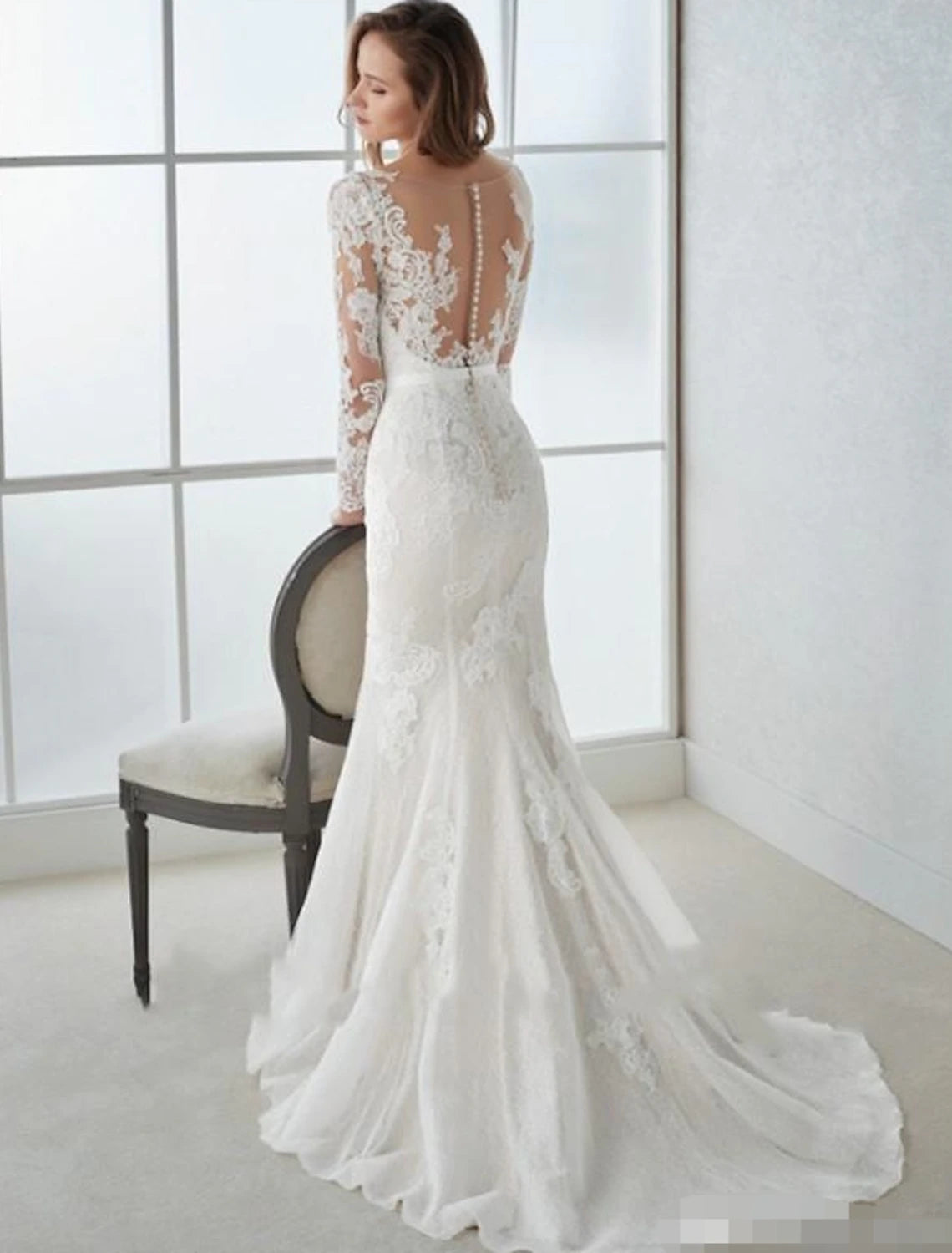 Close-up of the back of the elegant white mermaid V-neck long sleeve lace wedding dress, showing the open back and lace.