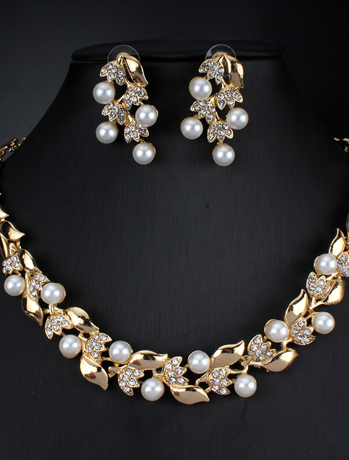 Woman wearing a white imitation pearl and rhinestone leaf necklace with matching hoop earrings.
