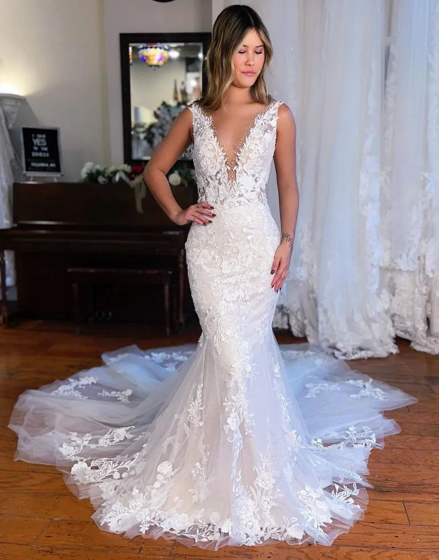 Woman wearing an elegant white mermaid wedding dress with deep V-neck, appliques, and chapel train.