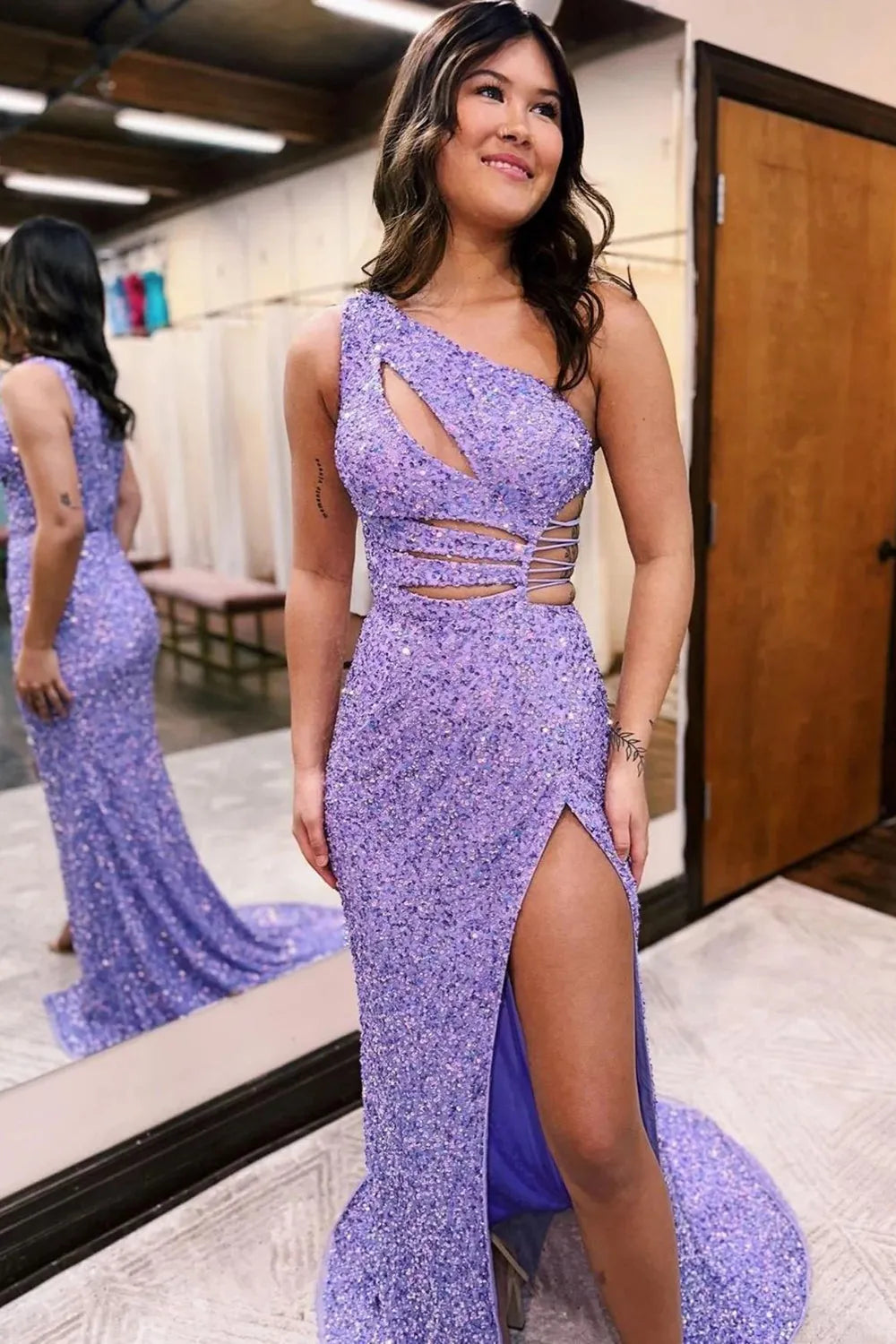 Woman wearing a glamorous one-shoulder sequined mermaid prom dress with a high front split.