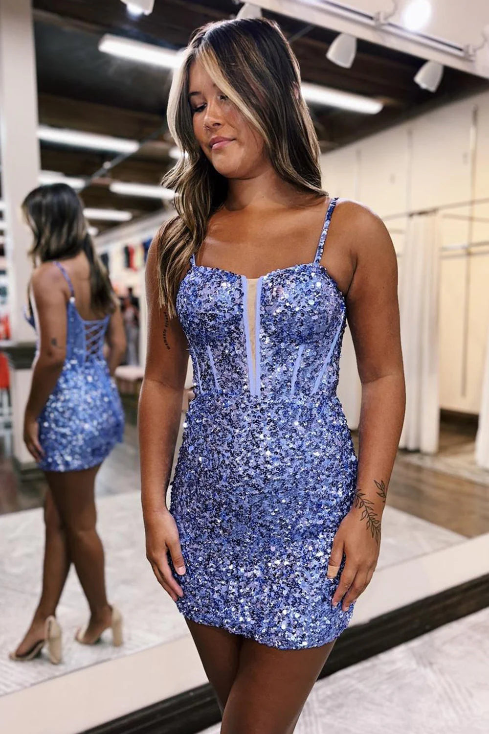 Model posing in a glittering short bodycon prom dress with spaghetti straps.