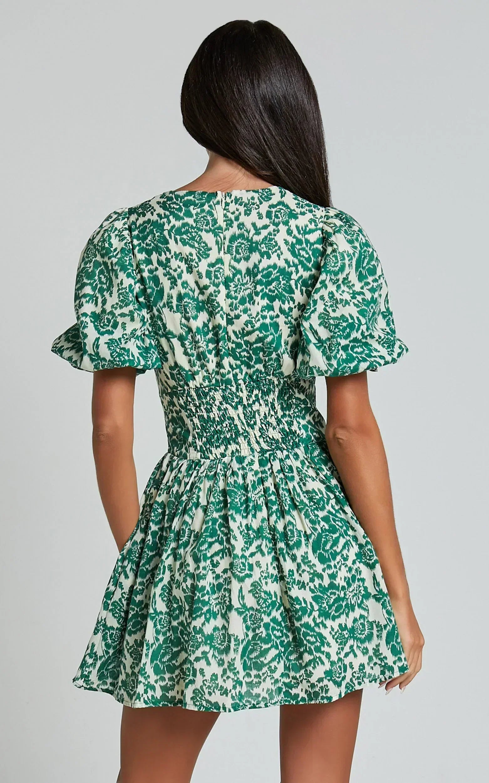 Back view of a woman in a green floral print mini dress with smocked waist.