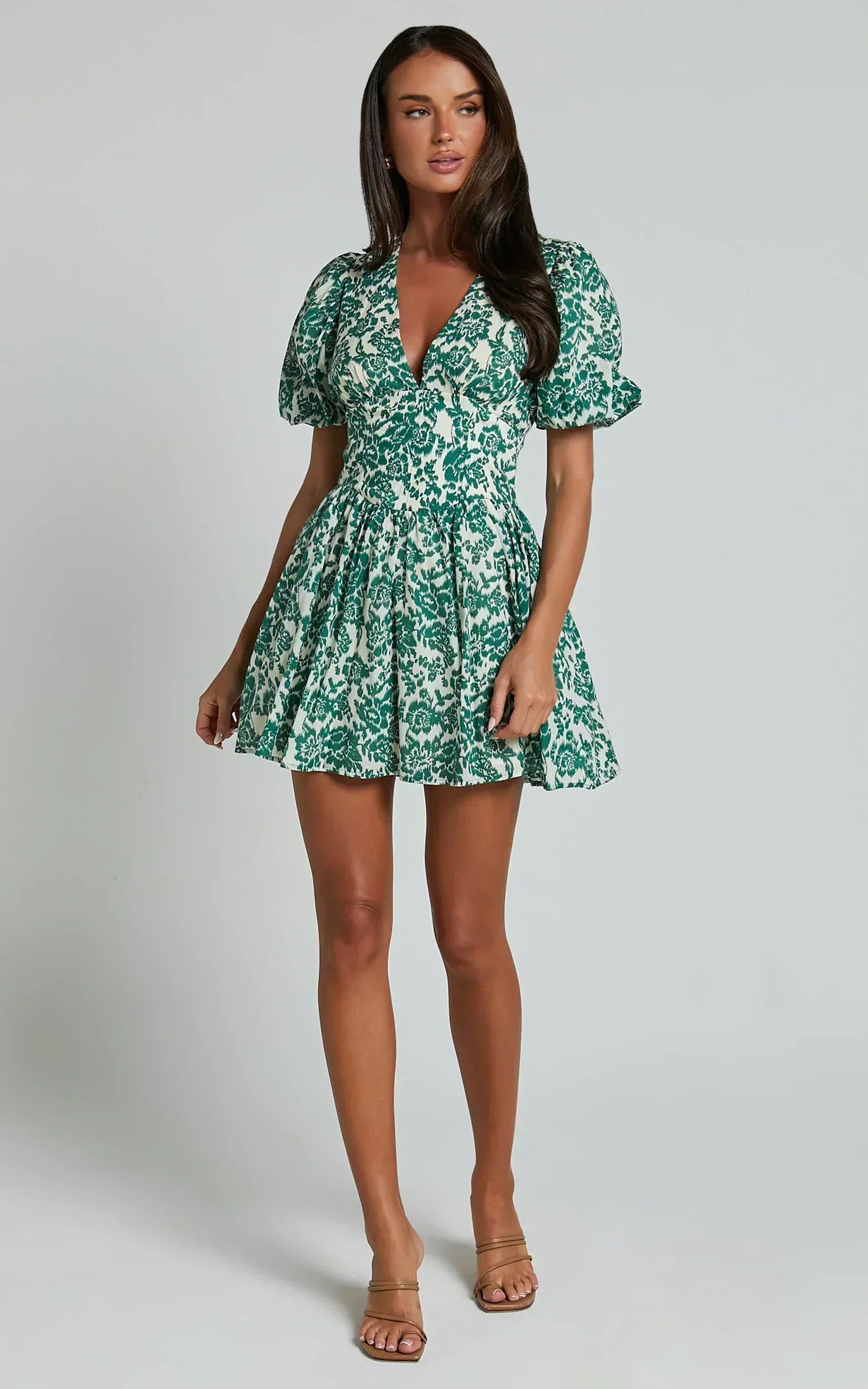 Side view of a woman showcasing the puff sleeves and A-line skirt of the green floral dress.