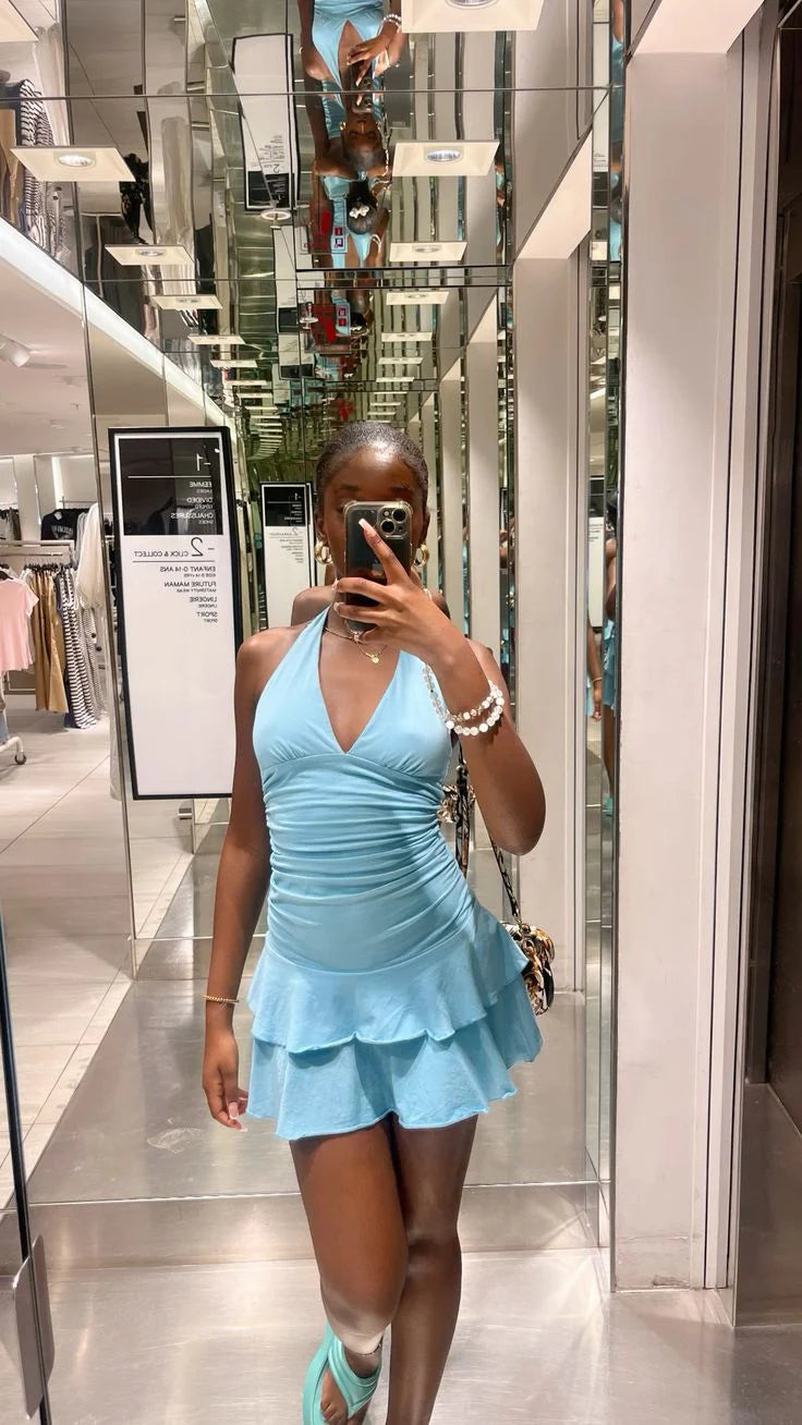 Woman wearing a light blue halter mini dress with a ruched bodice and tiered ruffle skirt.