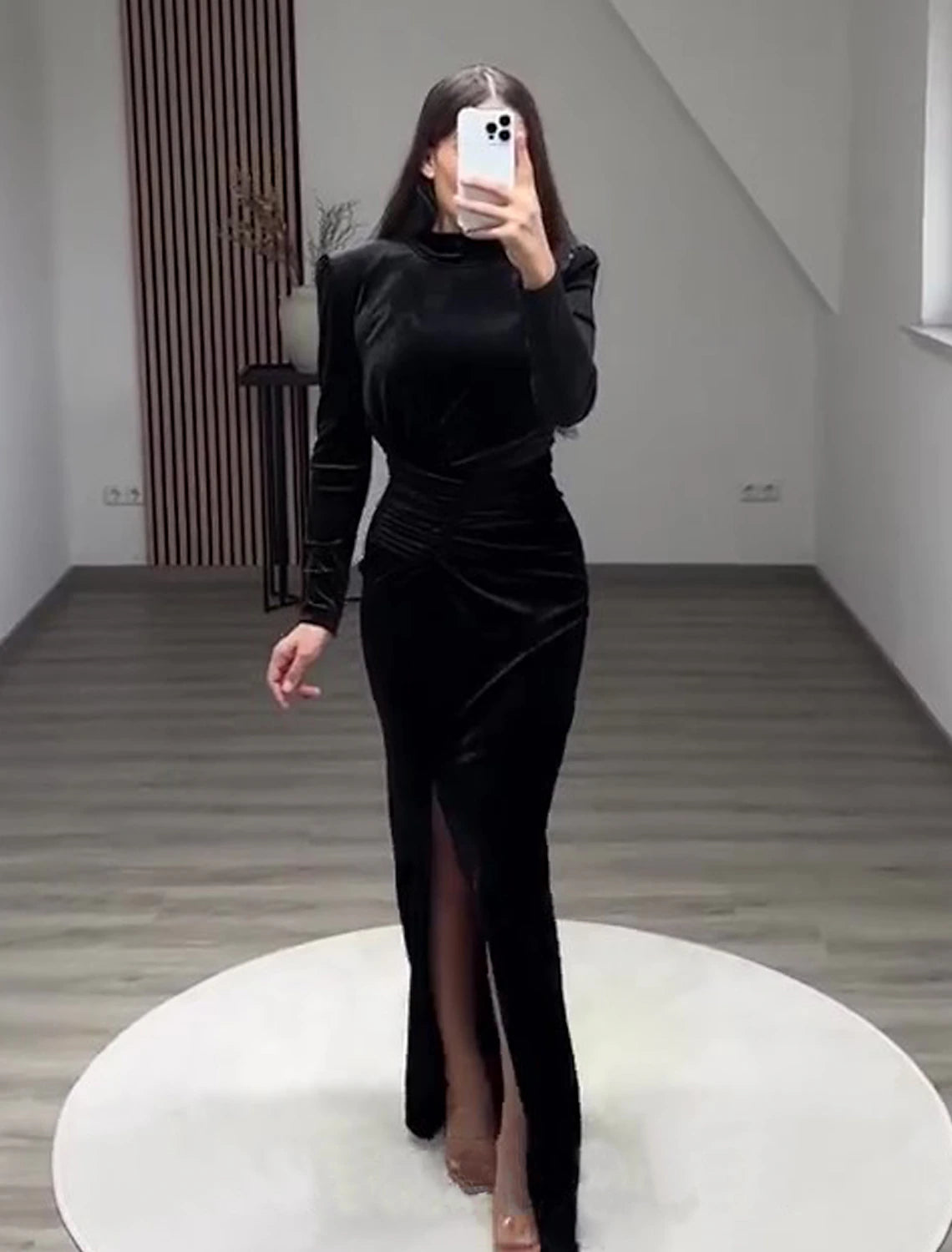 Woman wearing a black velvet high-neck long-sleeve sheath gown with a slit.
