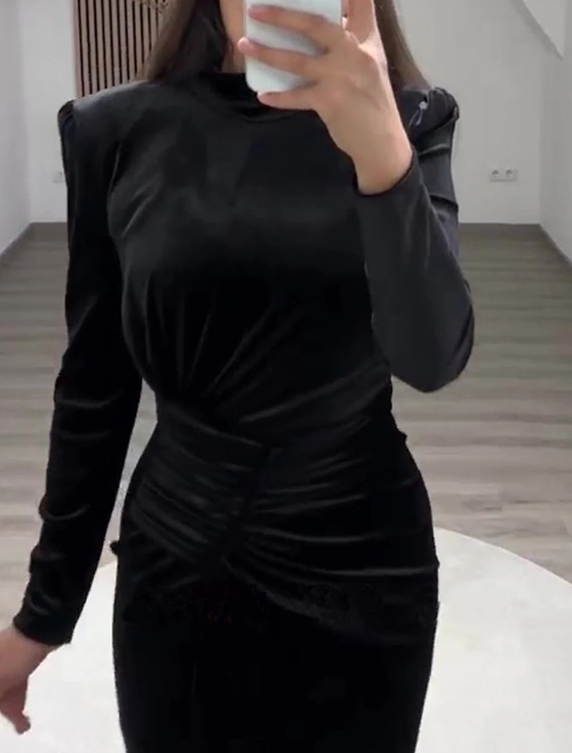 Back view of a woman in a black velvet high-neck long-sleeve sheath gown.