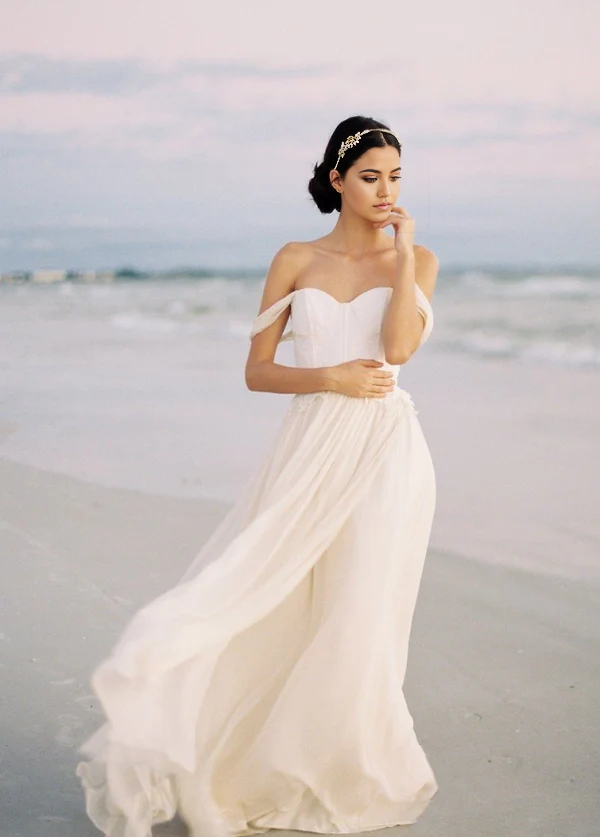 Model wearing A-line off-shoulder chiffon wedding dress with lace bodice and high slit.