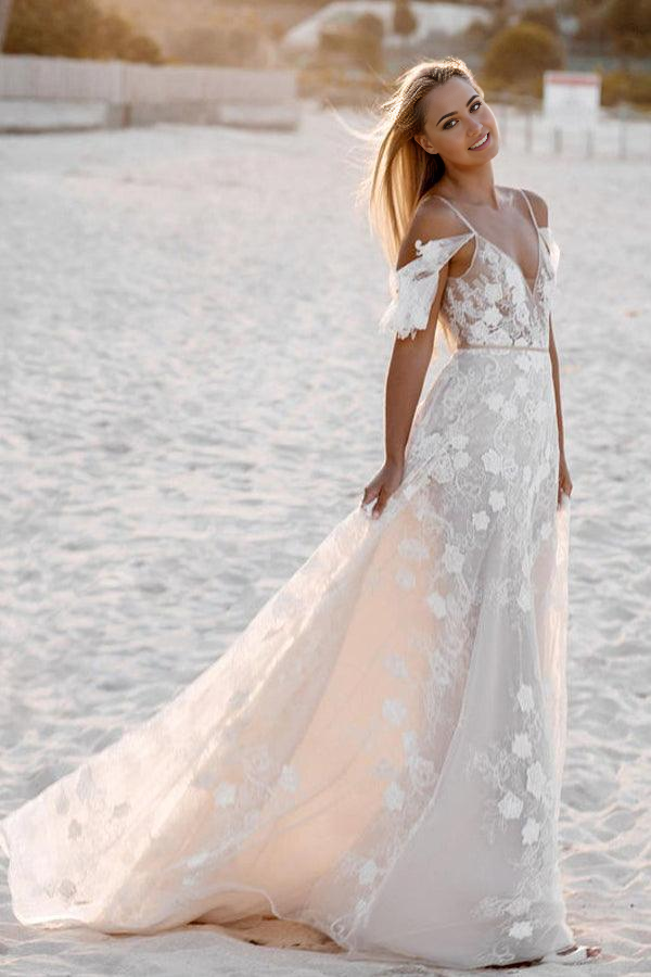 Model wearing a white floral lace spaghetti strap A-line wedding dress on a beach.