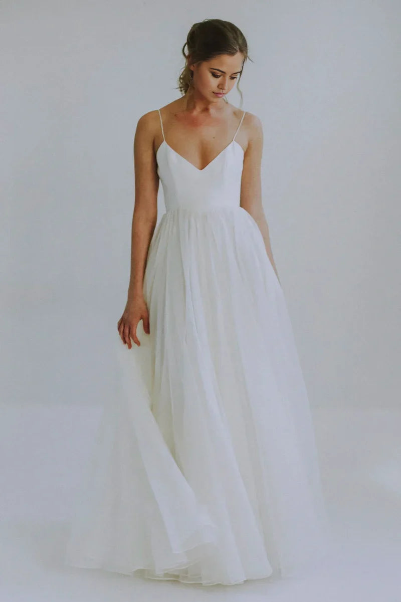 Bride wearing an elegant A-line V-neck wedding gown with spaghetti straps and a flowing tulle skirt.