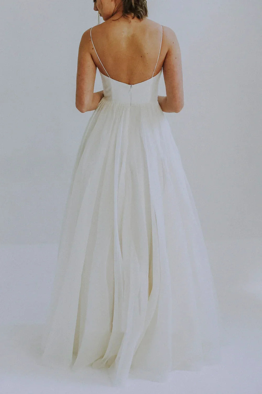 Full view of a bride in a romantic A-line wedding dress with spaghetti straps and a soft tulle overlay.