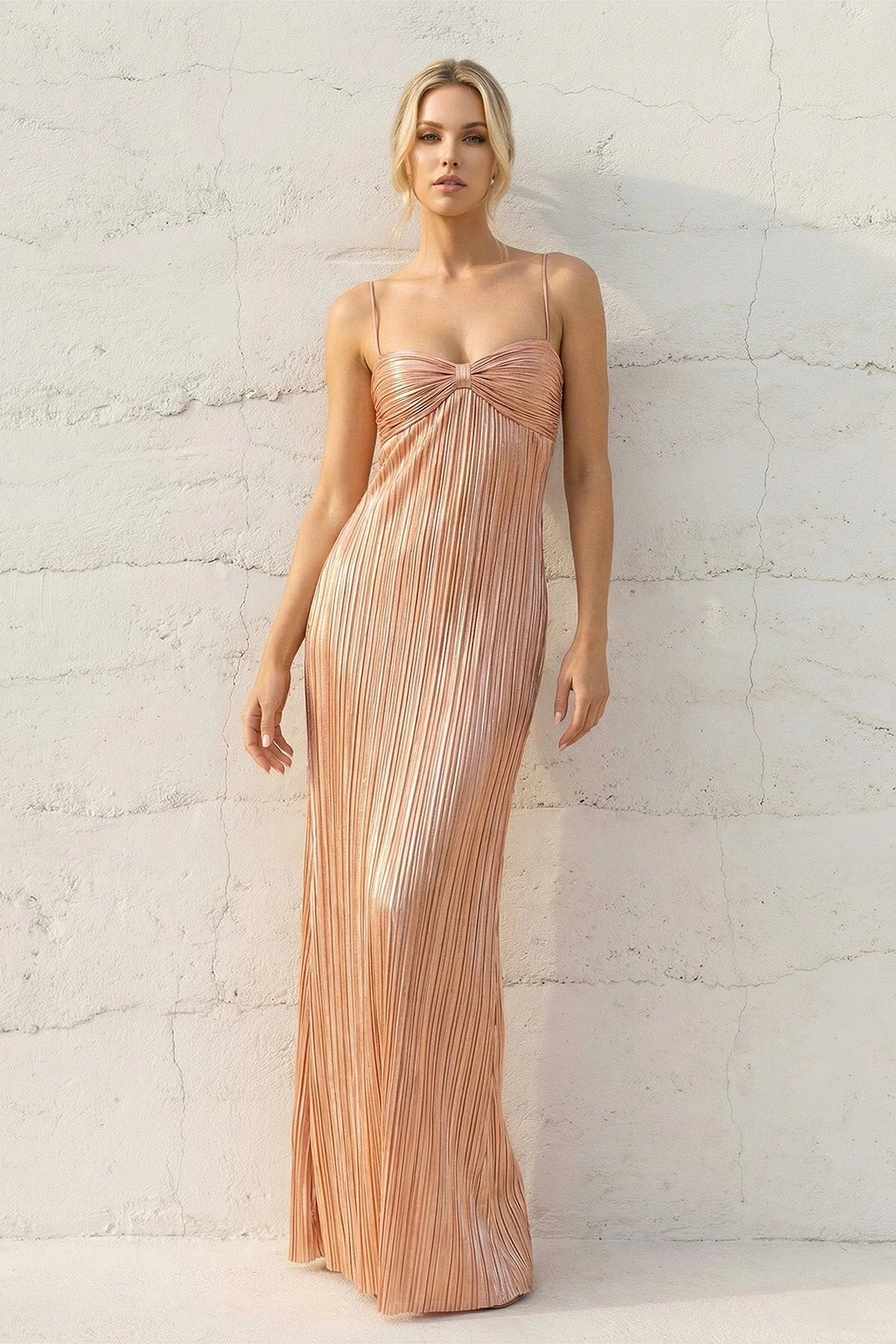 Model wearing a shimmering metallic pleated floor-length gown with spaghetti straps and a bow detail.