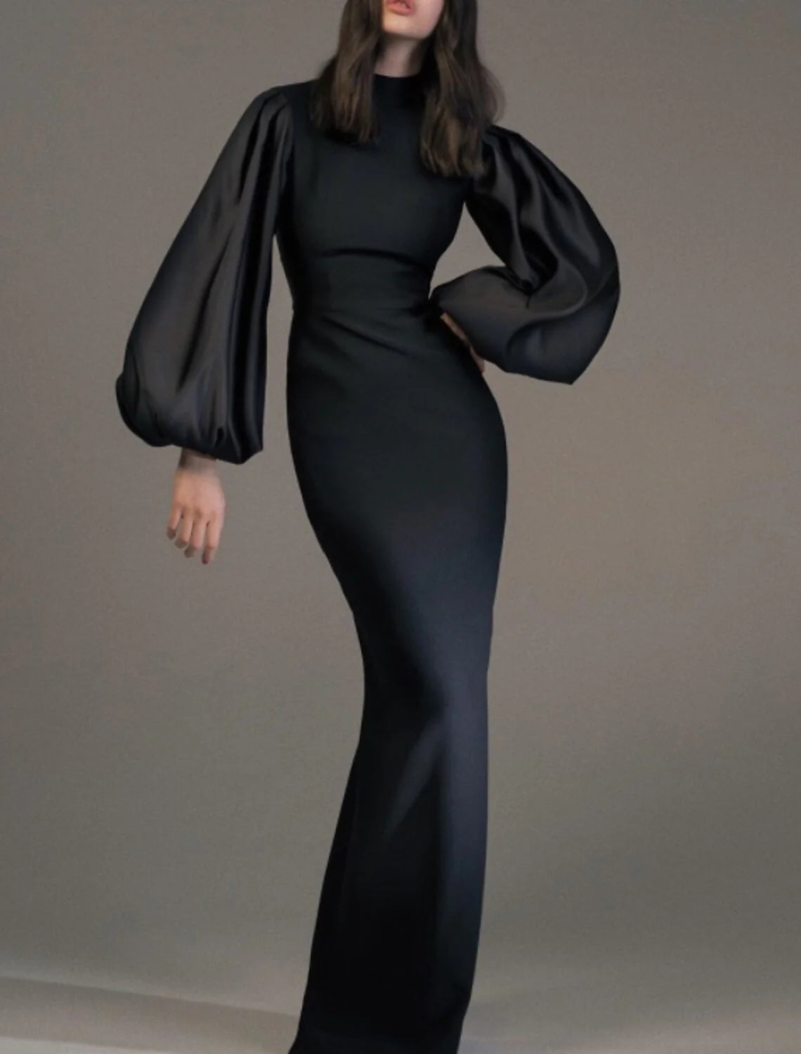 Back view of a model wearing a sophisticated black high-neck long-sleeve sheath evening gown.