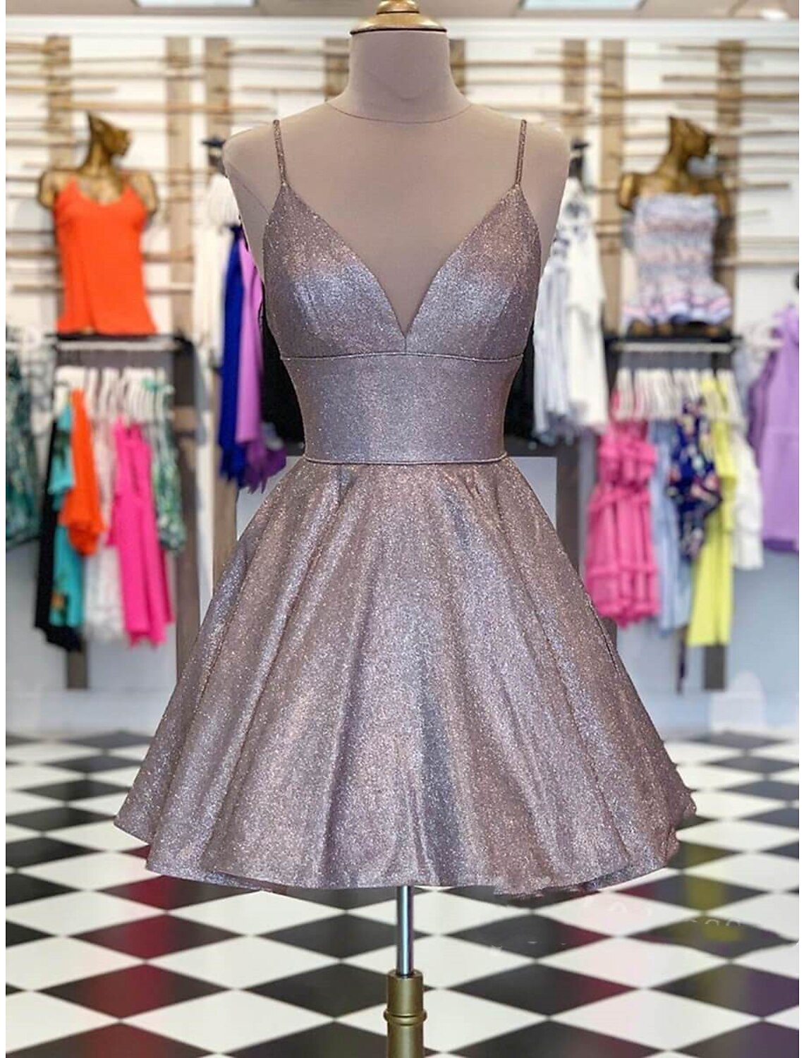 Woman wearing a sparkling A-line short homecoming dress with spaghetti straps and glitter.