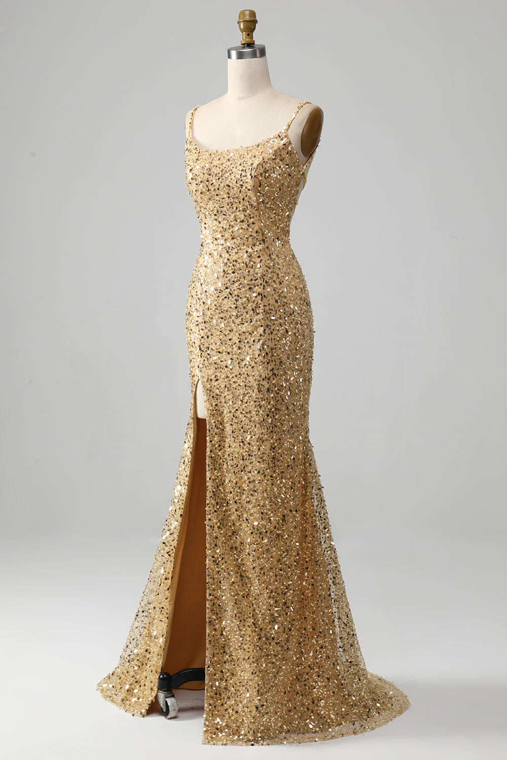 Woman wearing a golden sequined mermaid prom dress with spaghetti straps and a high slit.