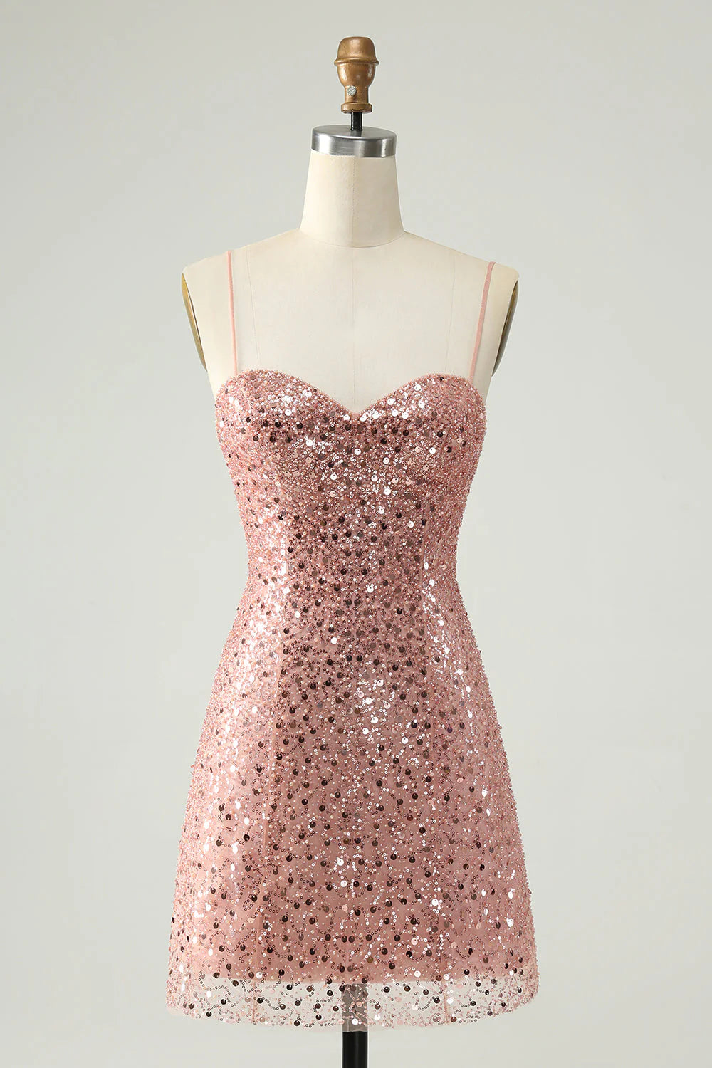 Woman wearing a blush sparkly A-line sequin cocktail dress with spaghetti straps.