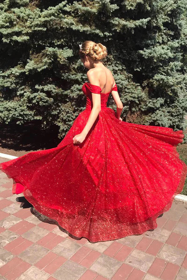 Full view of a woman wearing a sparkly red A-line off-shoulder tulle evening gown.