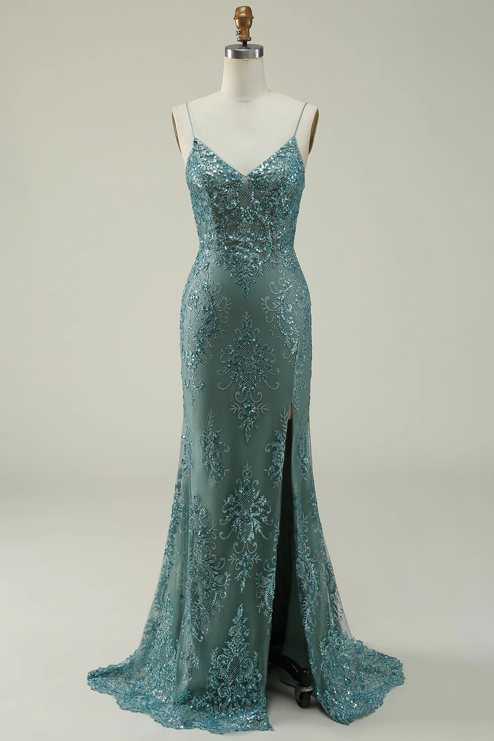 Woman wearing a sparkly green sequin long prom dress with spaghetti straps and a high slit.