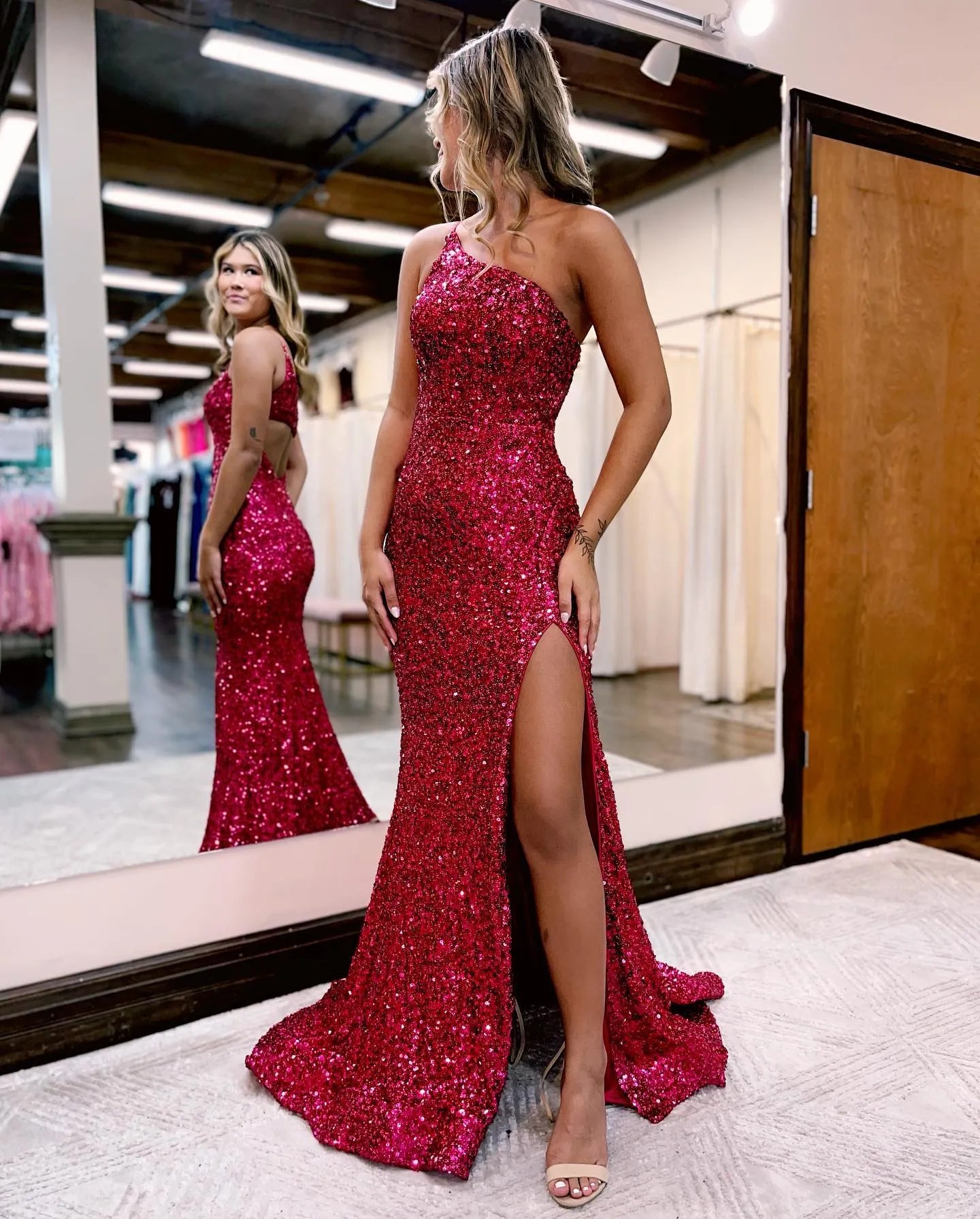 Model wearing a red glitter mermaid one-shoulder prom dress with a high slit.