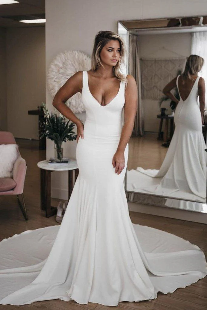 Bride wearing a simple mermaid V-neck wedding dress with a long train on a beach.