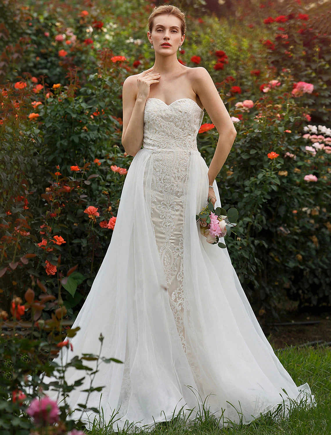 Full view of a bride wearing a sweetheart strapless mermaid wedding dress with lace appliques and a court train.