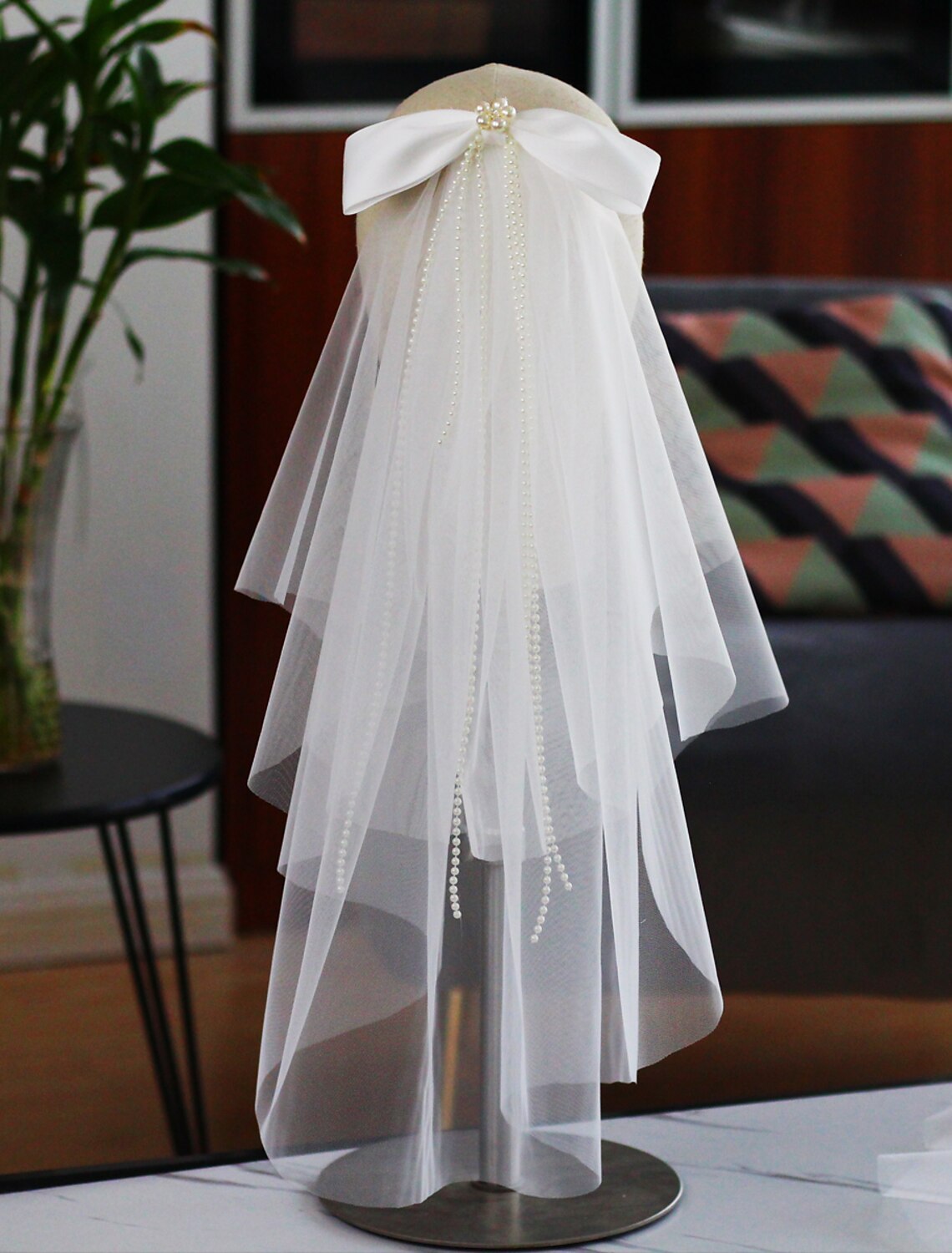 Bride wearing a two-tier elbow wedding veil with faux pearls and a satin bow, viewed from the front.