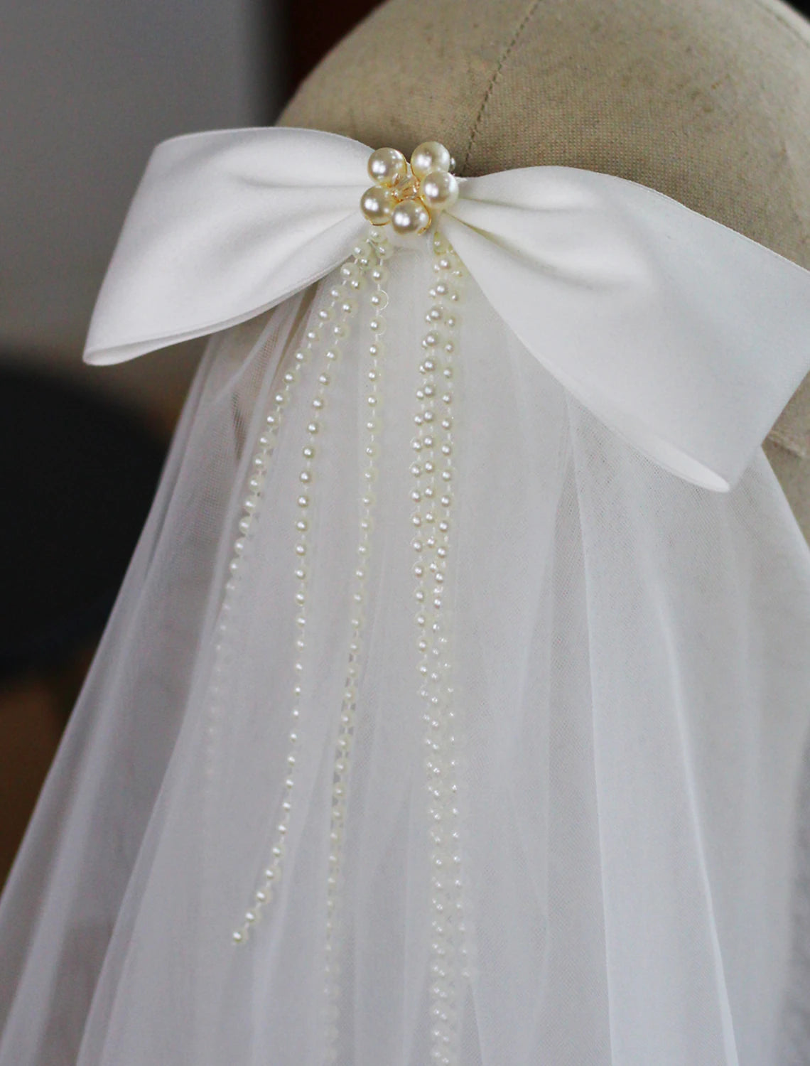 Close-up of the two-tier elbow wedding veil showing faux pearl details and satin bow.