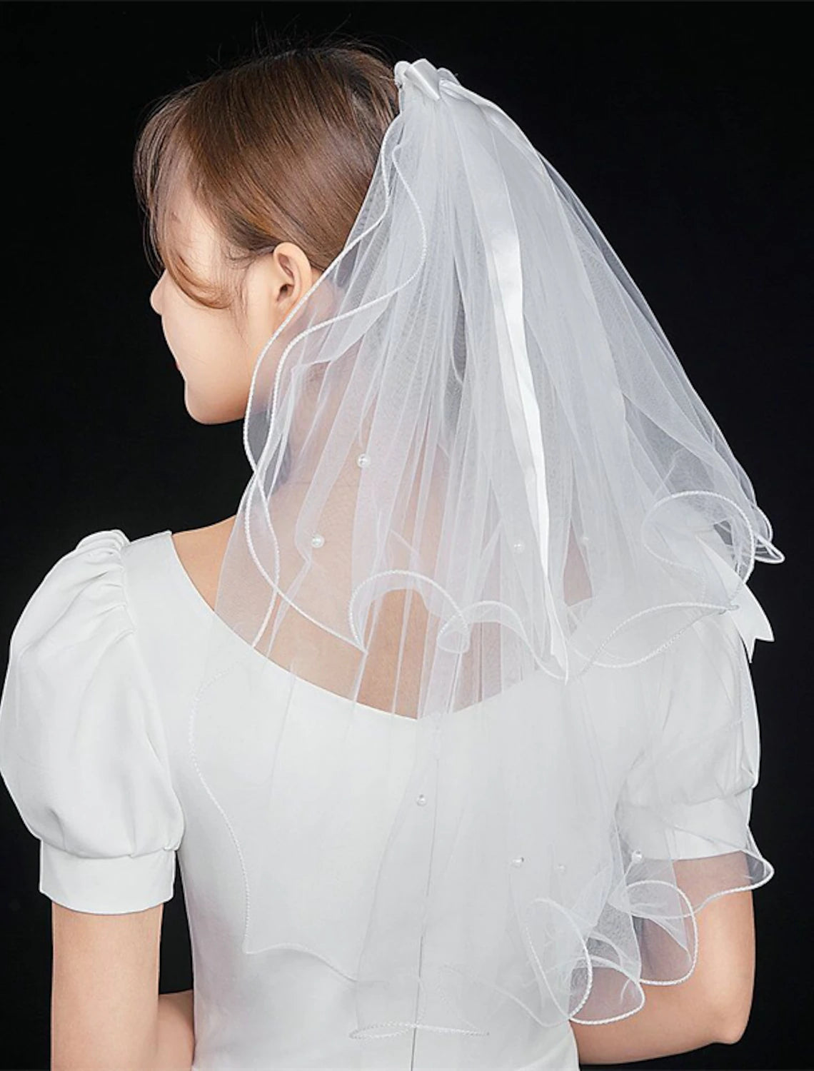 Bride wearing a two-tier elbow wedding veil with faux pearls and a satin bow.