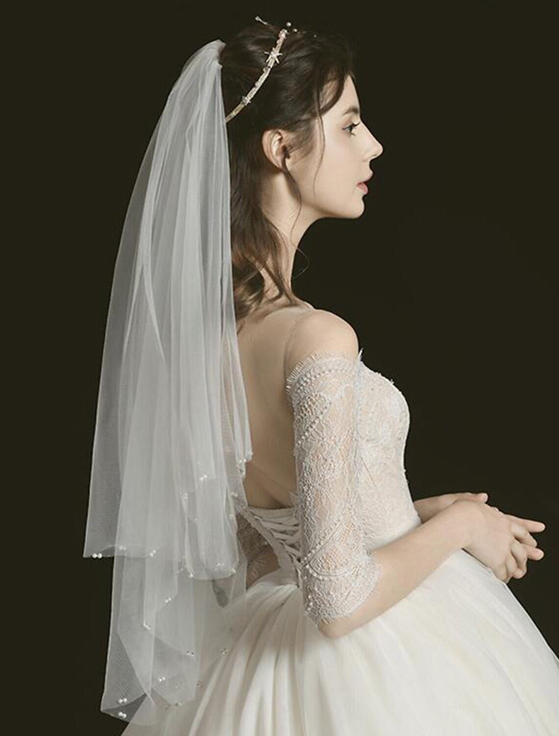 Bride posing with a two-tier elbow wedding veil featuring faux pearl details.