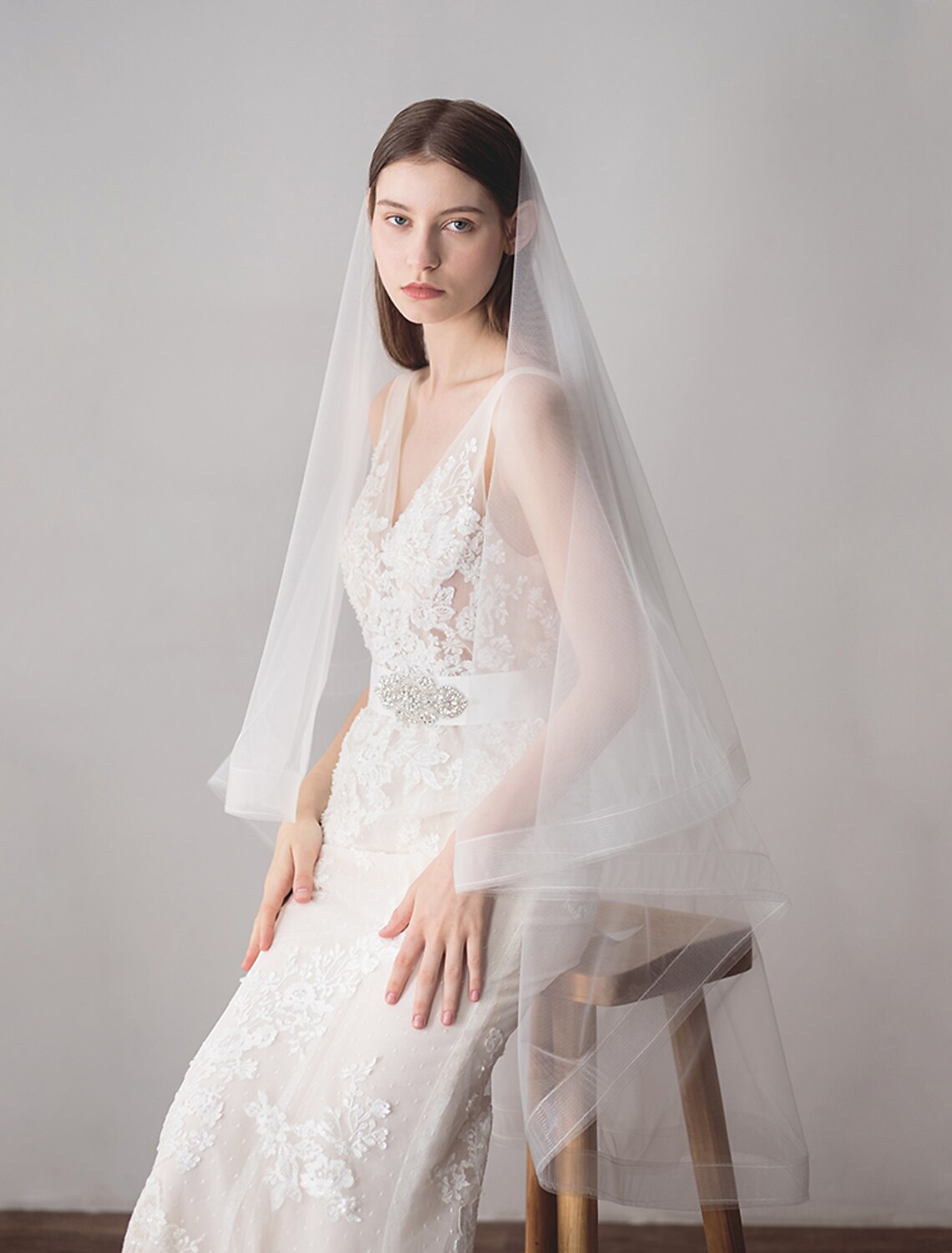 A bride wearing a two-tier fingertip wedding veil with fringe, looking elegant.