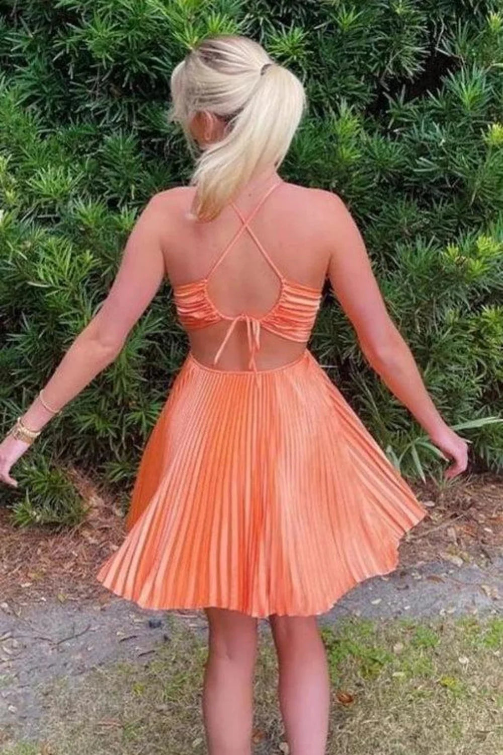 Back view of bright orange pleated mini dress with criss cross straps and cutouts.