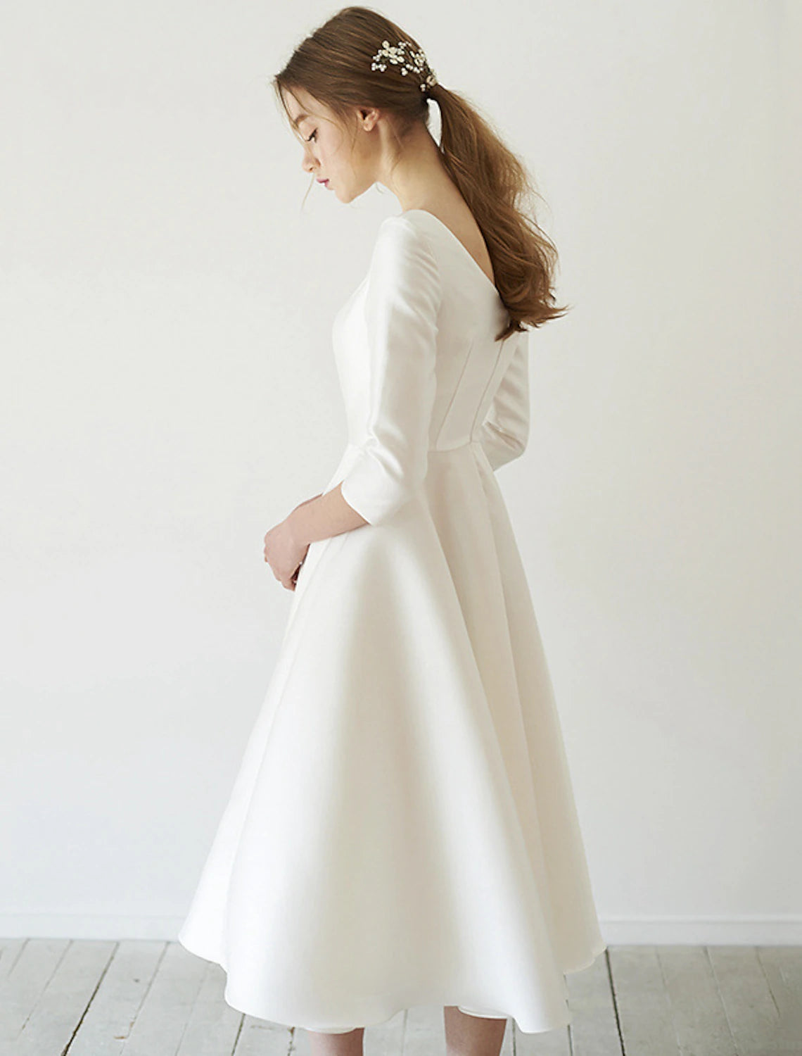 Side view of a vintage A-line satin wedding dress, showing tea length and pleats.