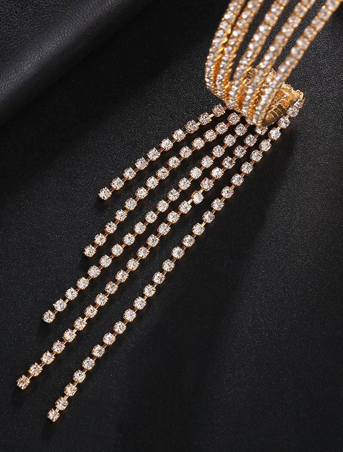 Women's gold rhinestone tennis bracelet with tassel fringe on a wrist.