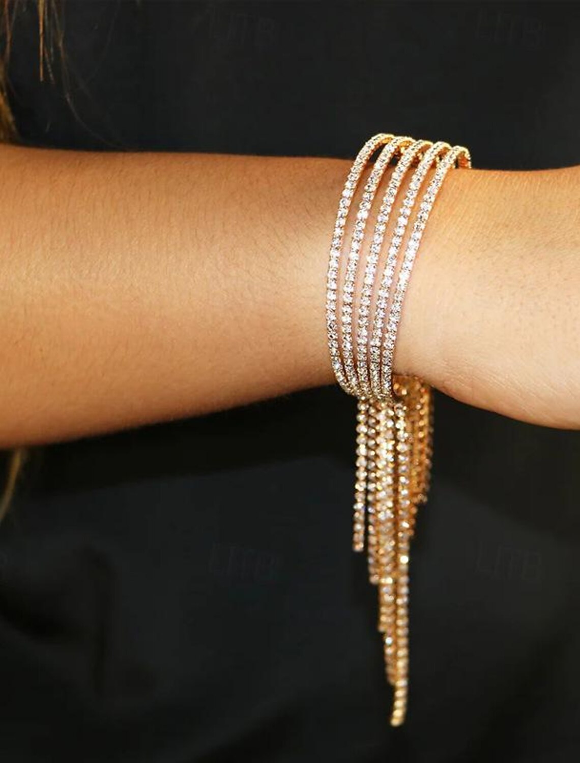 Stylish gold rhinestone bracelet with tassel fringe worn by a woman.