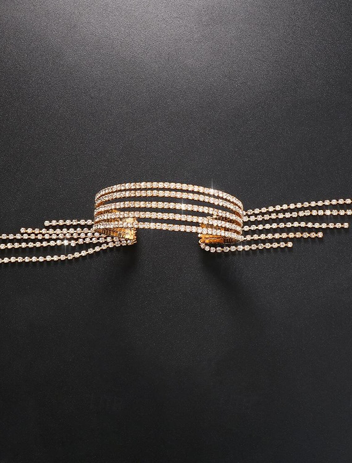 Gold tennis bracelet with rhinestones and flowing tassel fringe on a model.