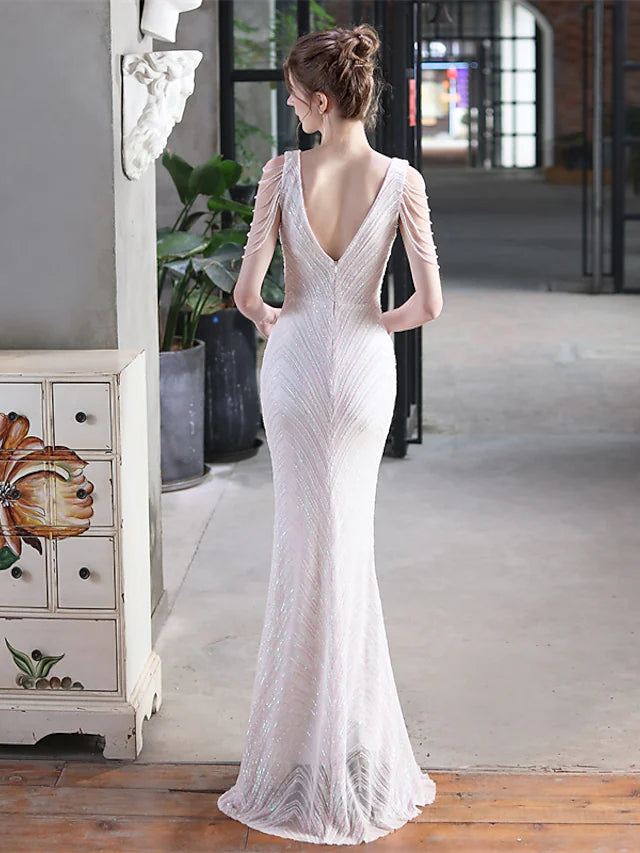 A woman posing in a sequined V-neck mermaid trumpet evening gown, showing the back.