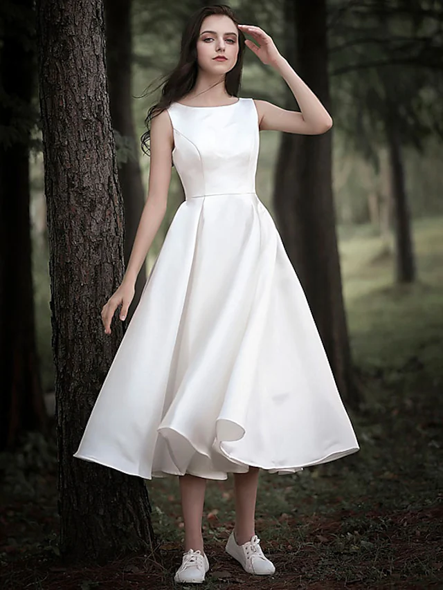 Model wearing an A-Line tea length wedding dress with jewel neck and cap sleeves.