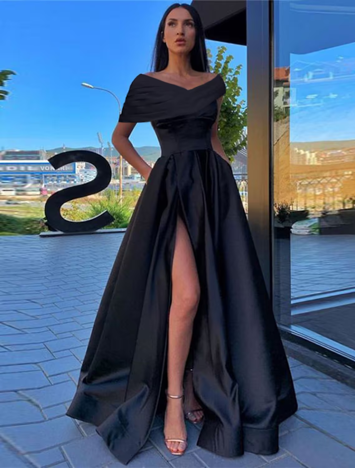 Model wearing an elegant A-Line off-shoulder black satin prom dress with a ruched slit.